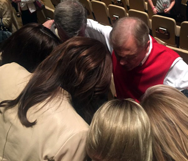 Ed Young (red sweater vest) prays with Caitlyn Jenner (tan coat)