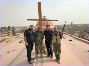 Father Ammar, another priest and two soldiers stand by a newly erected cross on the roof of Tahira church (church of the Immaculate, Syriac Catholic) in Qaraqosh, a Christian village liberated from IS. (World Watch Monitor)